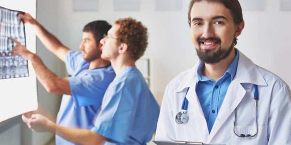 Portrait of friendly doctor looking at camera on background of his colleagues interacting